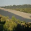 A landscape of the landfill appears in the middle ground, a brownish-sandy color, with trees at either side.