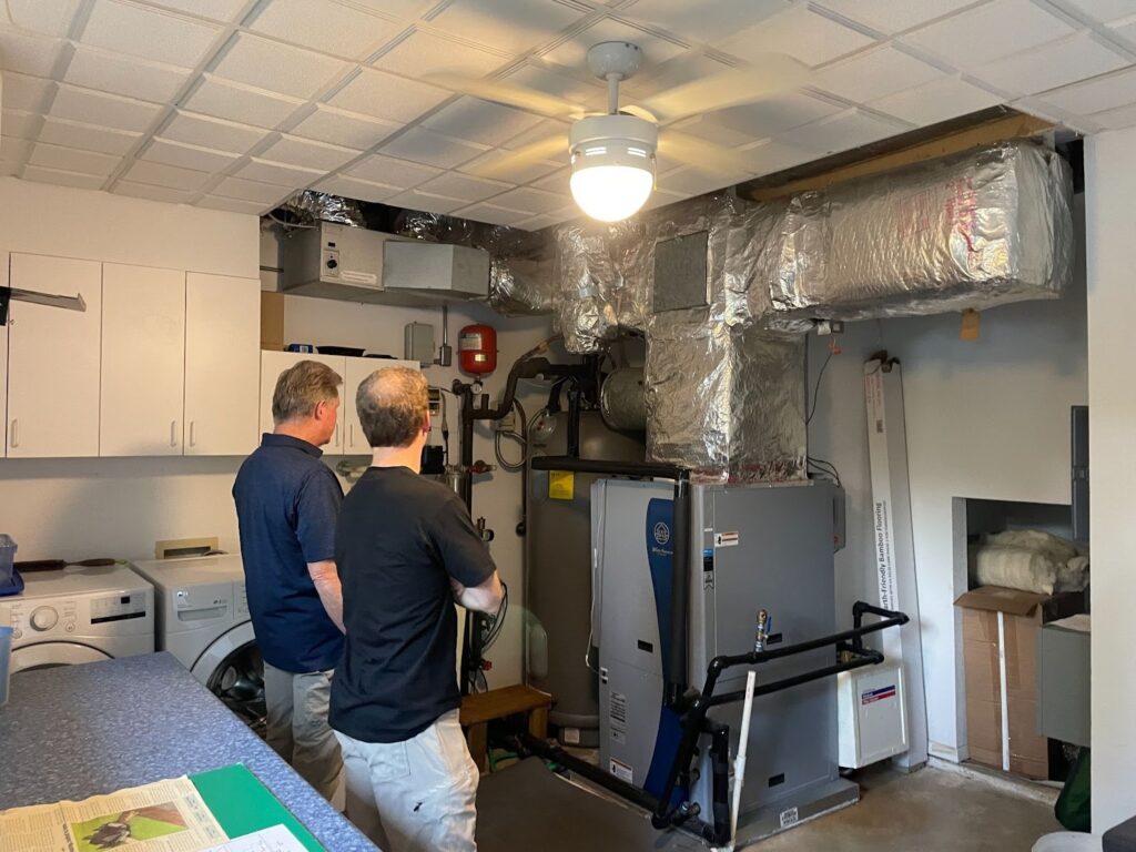 Two tour attendees examine the different systems the Westbrooks have put in place to heat and cool their home. Credit: Arcelia Martin/Inside Climate News