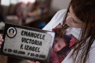 Pamela Rayane Fernandes holding a tombstone of her 5-year-old daughter Emanuelle, who died in Bento Rodriguez, Brazil, following the collapse of the Fundão mine dam in the mountains of southeast Brazil nine years ago. Credit: Douglas Magno/AFP via Getty Images