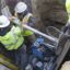 The photo show workers in hard hats and reflective vests in a trench with equipment.