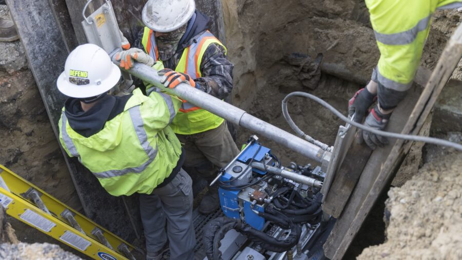 The photo show workers in hard hats and reflective vests in a trench with equipment.