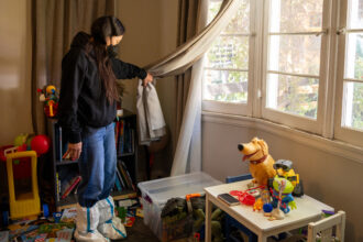 Adriana Valdez pulls back a drape to inspect the layer of ash coating her son’s toys at her home in Altadena on April 1.