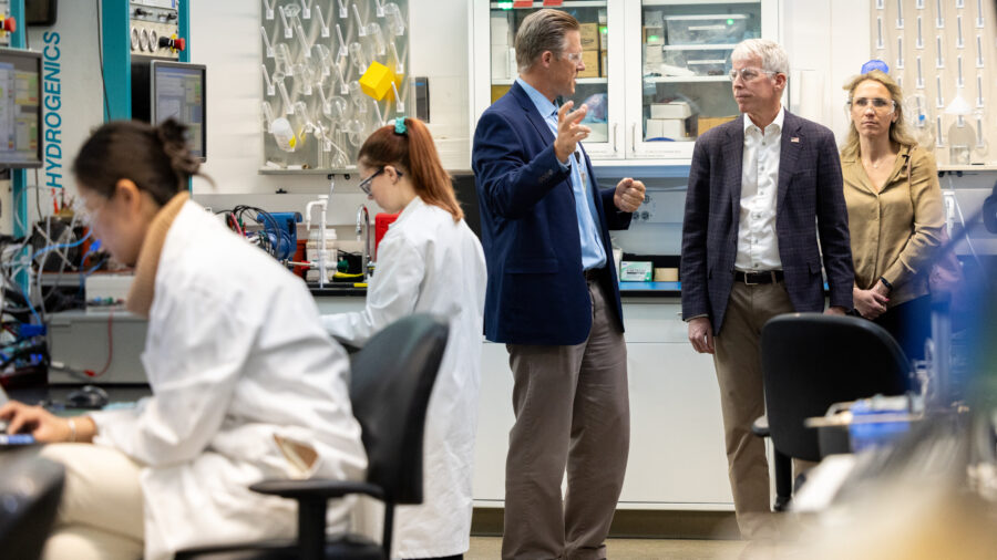 Chris Wright is inside a lab, talking to people standing near scientists in lab coats.