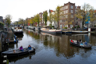 People navigate small boats through the Lekkersluis canal in Amsterdam. Credit: Nick Gammon/AFP via Getty Images