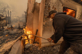A man uses a wrench stuck into a pipe to turn off a burning gas line during the Eaton Fire on Jan. 8 in Altadena, Calif. Credit: David McNew/Getty Images