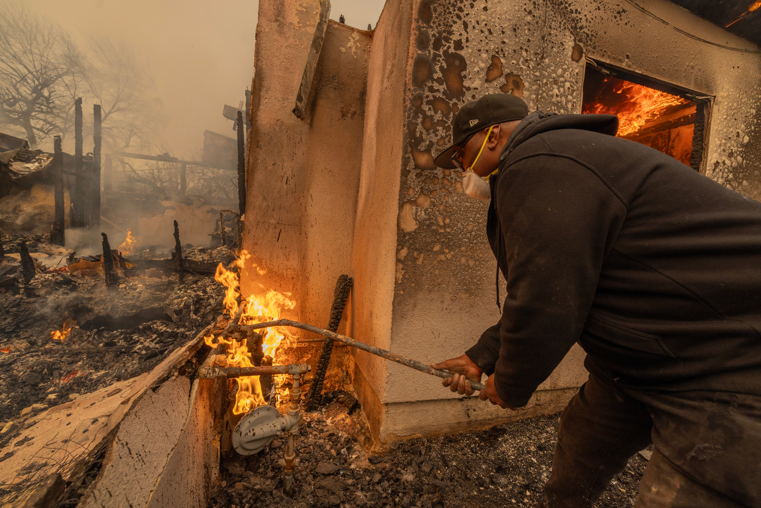 A man uses a wrench stuck into a pipe to turn off a burning gas line during the Eaton Fire on Jan. 8 in Altadena, Calif. Credit: David McNew/Getty Images