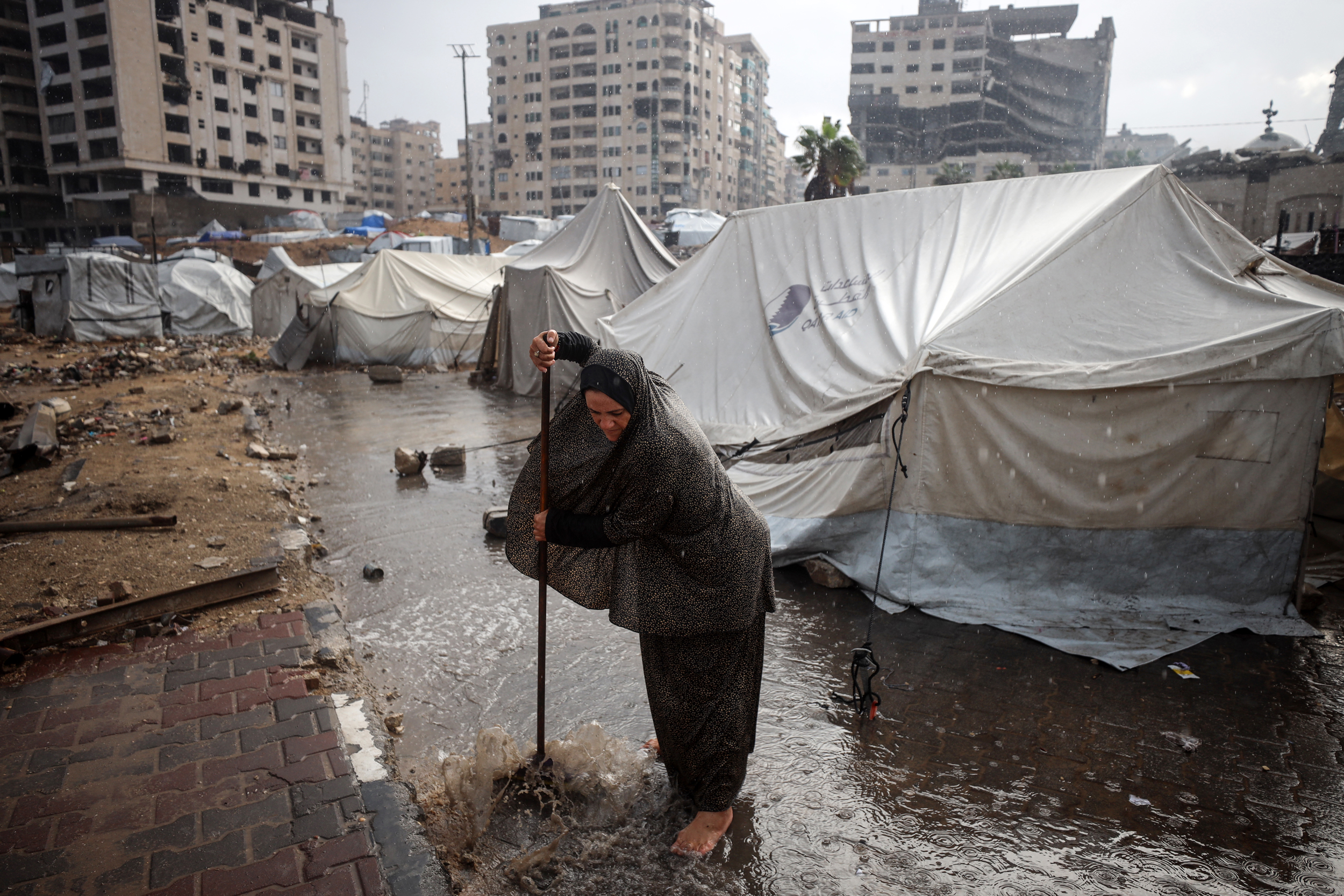 A displaced Palestinian woman pushes water away from her tent after heavy rainfall at a makeshift camp inside Gaza’s port on Nov. 14. Credit: Majdi Fathi/NurPhoto via Getty Images