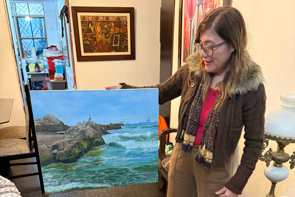 Miriam Arce, an artist and shop owner who has lived in the same house in Chancay since she was a baby, displays one of her paintings of the coastline that is now home to the Chinese-majority-owned Chancay megaport. Credit: Georgina Gustin/Inside Climate News