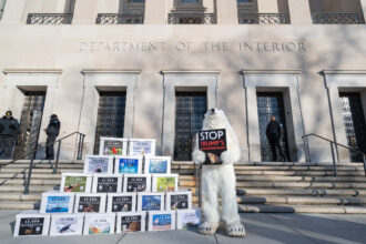 The environmentalist is holding a sign that says, “Stop Trump’s Extinction Plan.”