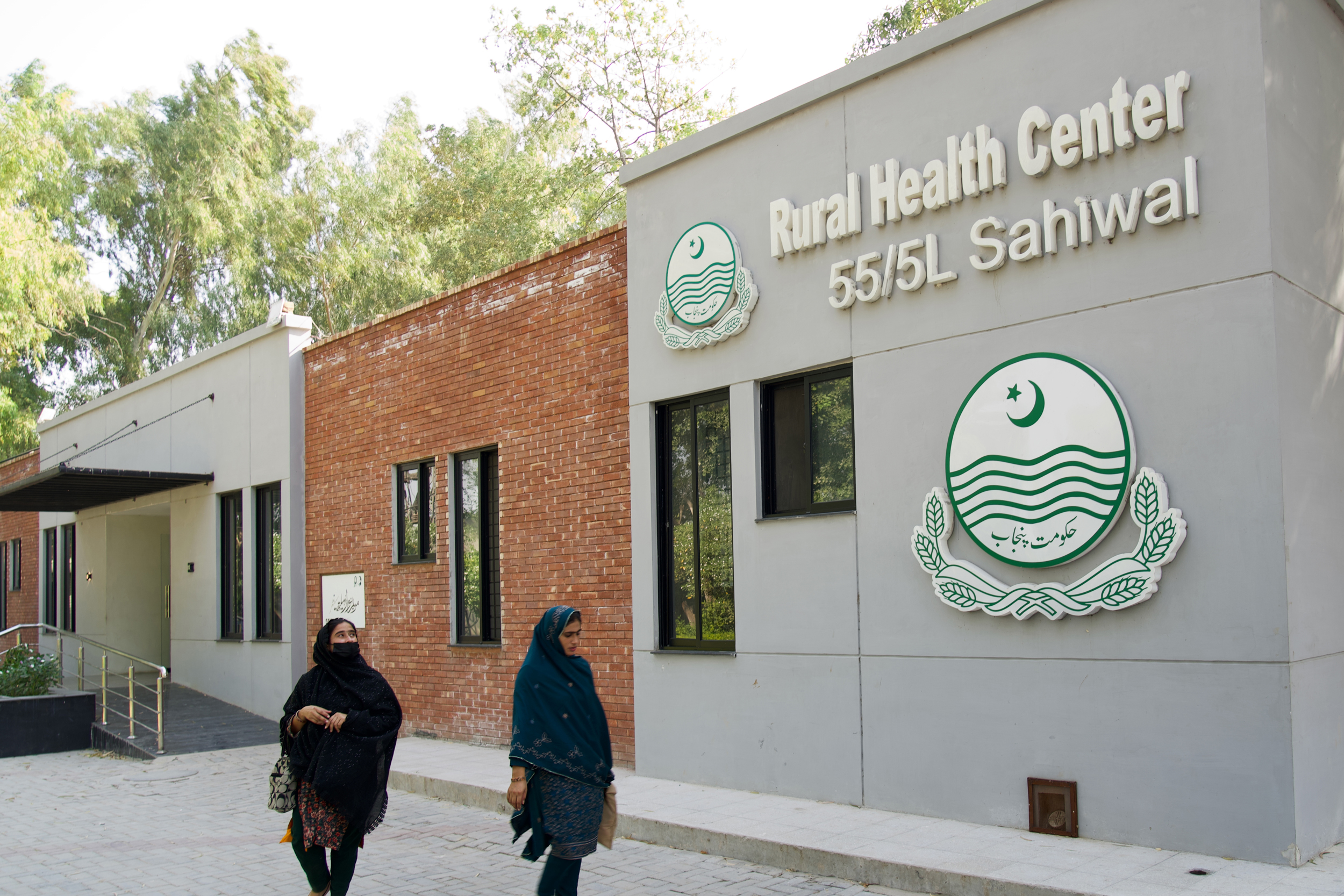 Women walk past the Rural Health Center in village 55/5L, where clinic records show a rise in respiratory and skin-related illnesses since the nearby Chinese-financed coal power plant began operating. Credit: Aman Azhar/Inside Climate News