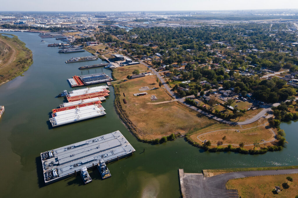 An aerial photo shows the river and the homes nearby. Many barges are near the river's edge in the water.