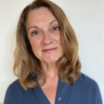In a headshot photo, Christine Spolar is smiling at the camera. She has shoulder-length light brown hair and is waring a blue shirt.