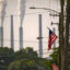 White-gray emissions billow from the stacks in the background. In the foreground is an American flag on a telephone pole.