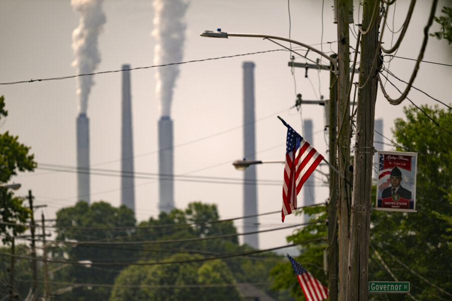 White-gray emissions billow from the stacks in the background. In the foreground is an American flag on a telephone pole.