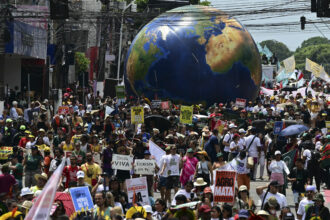 An inflatable that looks like the Earth rises above a mass of people, some carrying signs, including, "We are Nature, Nature is Us"