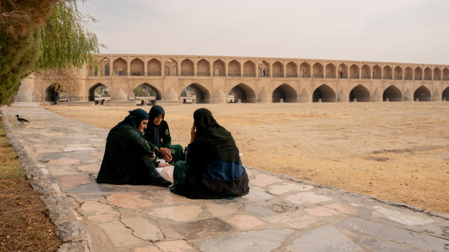 Women sit on a sidewalk along the dried-up riverbed of the Zayanderud in Isfahan, Iran, on Dec. 1, 2025. Credit: Hozi/Middle East Images/AFP via Getty Images
