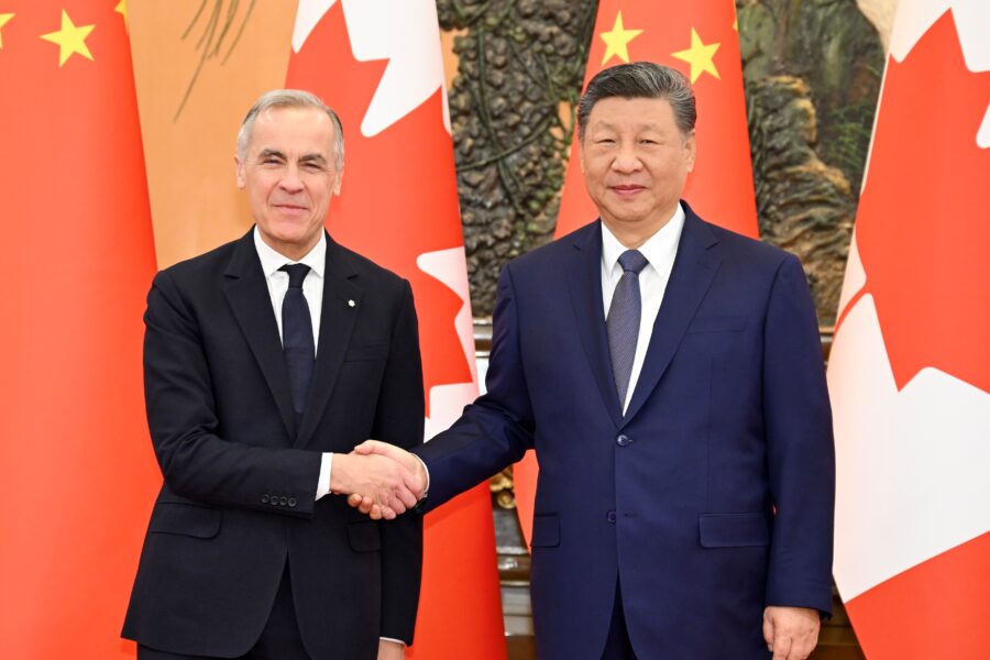 Chinese President Xi Jinping and Canadian Prime Minister Mark Carney shake hands while smiling at the camera, their country's flags behind them.