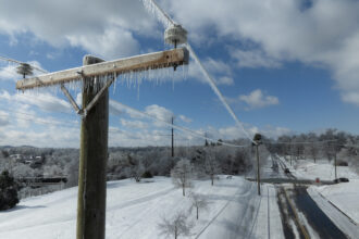 Utility lines with ice stretch over a snowy scene with a plowed road.