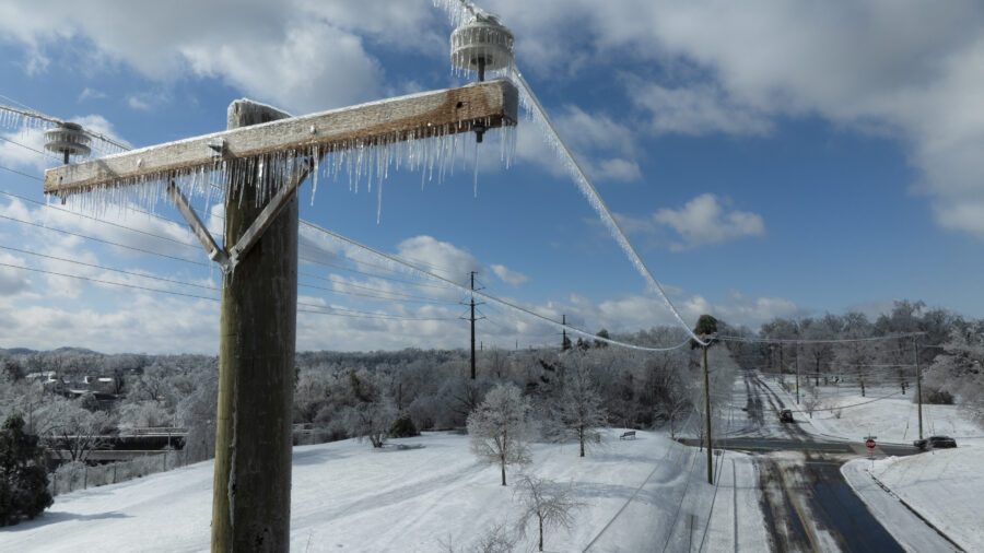 Utility lines with ice stretch over a snowy scene with a plowed road.