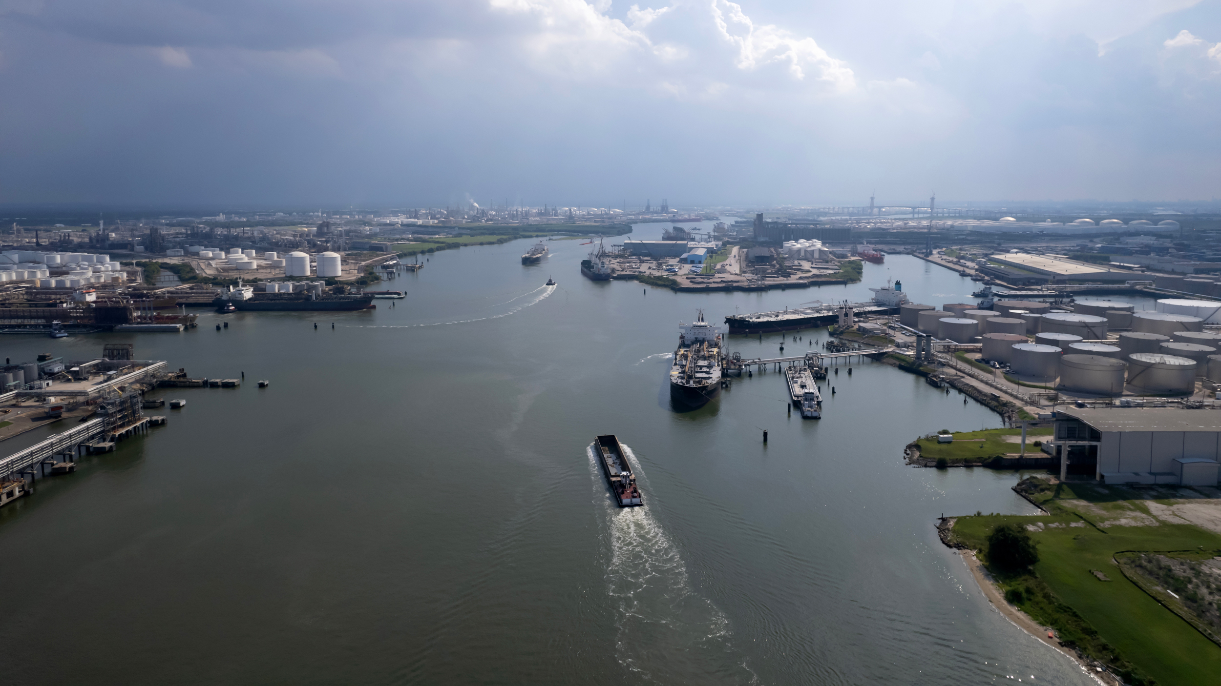 An aerial shot shows the barge and tug boat on the waterway under a blue sky with clouds.