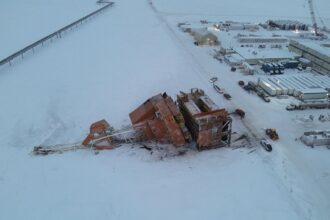 An aerial photo shows the oil rig collapsed in the snow next to a snowy road, emergency vehicles and an industrial complex