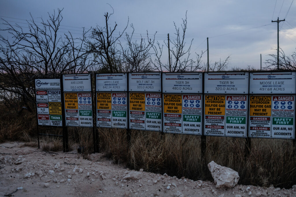 Signs for oil lease sites are posted next to warning signs for poisonous gas along Frying Pan Ranch Road, at the T-Bar Ranch in Winkler County, Texas, on Nov. 19, 2025. Credit: Paul Ratje/Inside Climate News