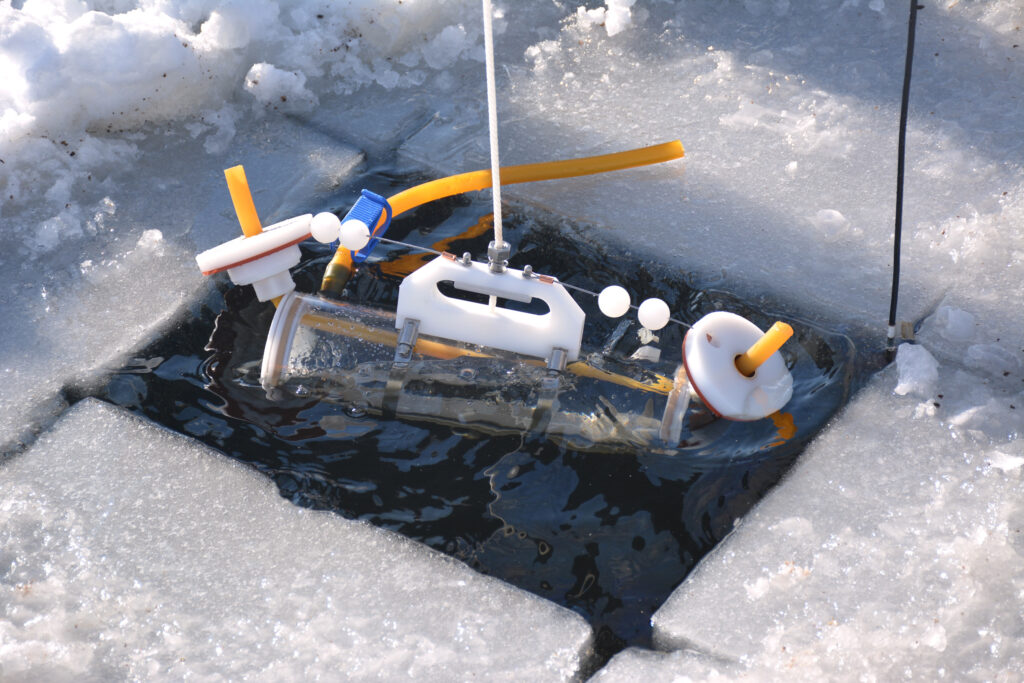 Lake Stewards of Maine volunteers use a Van Dorn bottle to capture water samples from different depths of a frozen-over Highland Lake. Credit: Sydney Cromwell/Inside Climate News