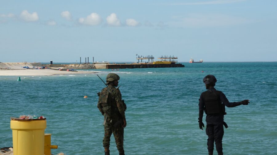 The police officer and solider are in the foreground; beyond them, water stretches out toward the project.