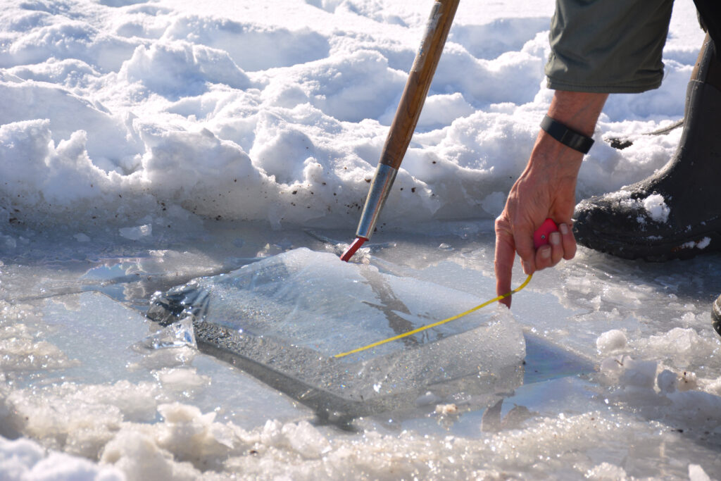 A volunteer measures the ice thickness in Highland Lake before conducting water-quality testing. The ice measured 11 inches thick in late January. Credit: Sydney Cromwell/Inside Climate News