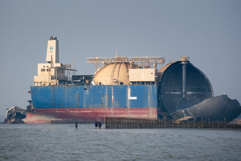 Local men check their fishing traps in the shadow of a half-cracked LNG (Liquefied Natural Gas) dome. Credit: Spencer Call/NGO Shipbreaking Platform.