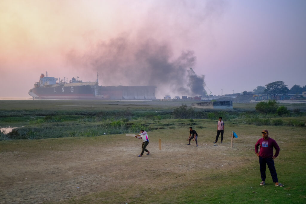 Locals play cricket in front of the smoke-filled ship graveyard at Sitakunda, Bangladesh. Credit: Spencer Call/NGO Shipbreaking Platform.