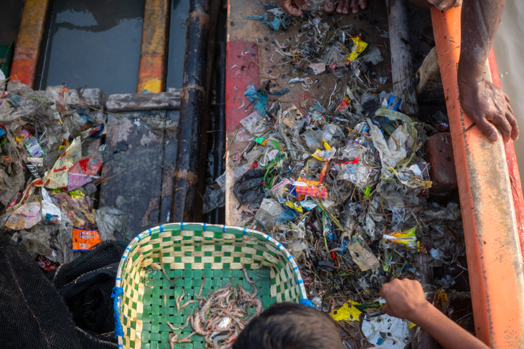 Fishermen pluck shrimp from piles of trash inside the hull of a repurposed emergency lifeboat. Credit: Spencer Call/NGO Shipbreaking Platform.