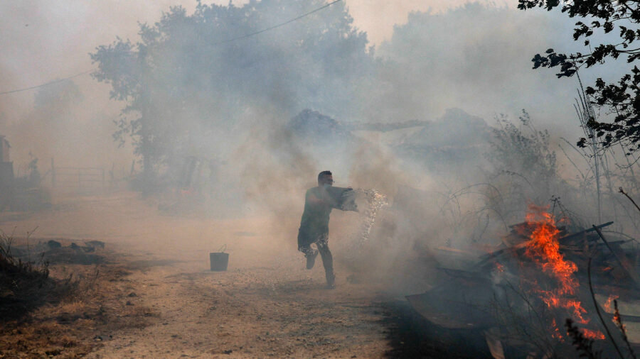 A man uses buckets of water to extinguish a wildfire that threatens his house in the Portuguese village of Antas on Aug. 15, 2025. Credit: Patricia de Melo Moreira/AFP via Getty Images