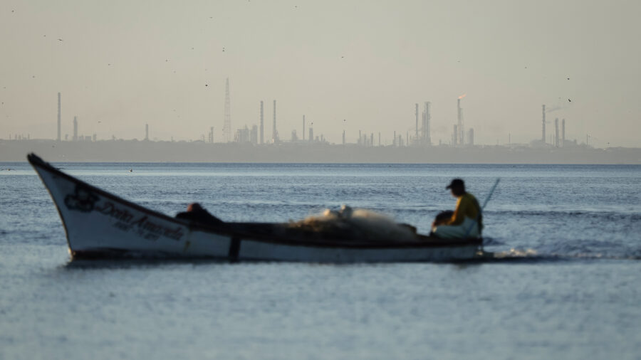 The Punta Cardon oil refinery is seen in the background of a fisherman sailing his boat from a beach in Amuay, Venezuela. Credit: Jesus Vargas/picture alliance via Getty Images