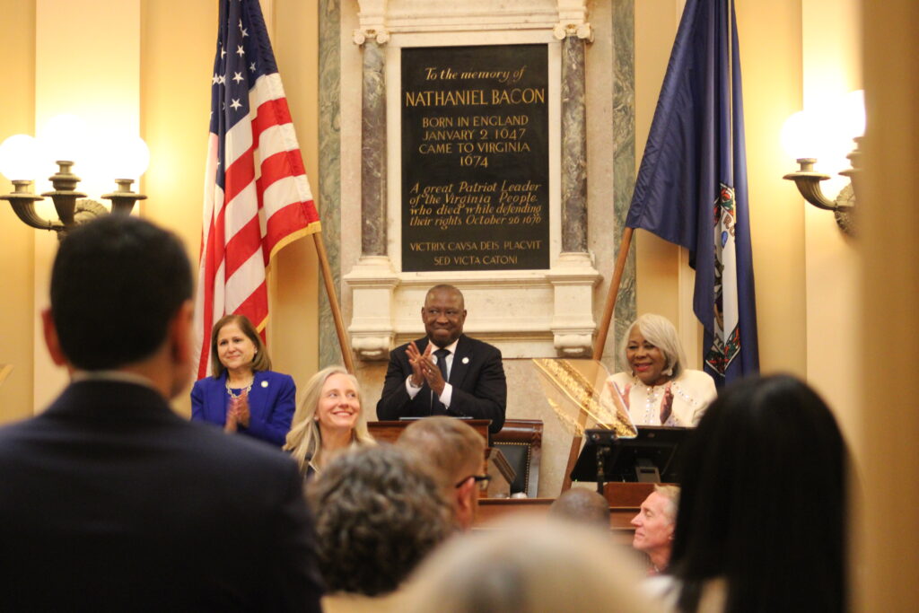 The photo is indoors beside flags and a sign about Nathaniel Bacon, who arrived in Virginia in 1674.
