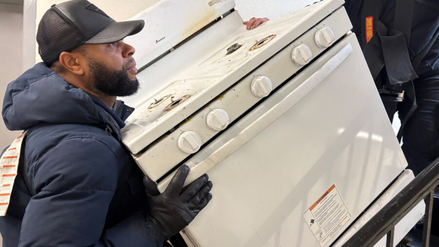 Workers remove an old stove from a Bronx apartment as part of a full-building induction stove installation in New York City. Credit: Lauren Dalban/Inside Climate News