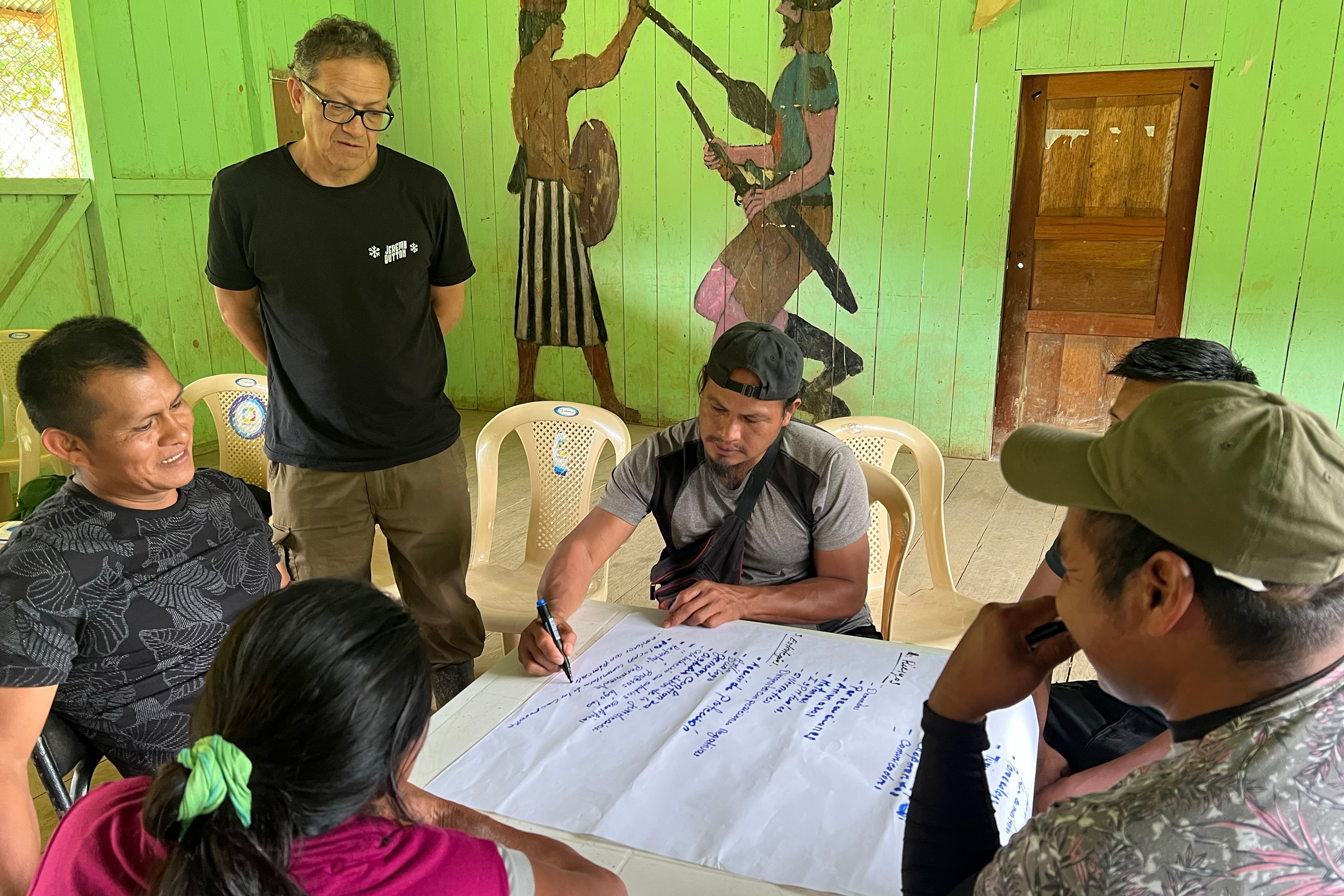 Sergio Nantip and Edwin Zárate watch as paraecologist Claudio Ankuash Nantip writes down ideas for the Ecoforensic program.