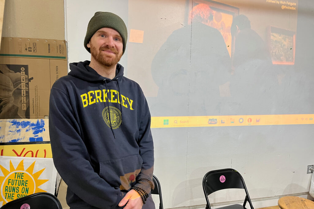 Nate Smith, an organizer with Extinction Rebellion NYC, stands in front of a projection of European activists preparing to splatter a Vincent van Gogh painting with soup, an action Smith would soon analyze with a group as part of a training. Credit: Nicholas Kusnetz/Inside Climate News