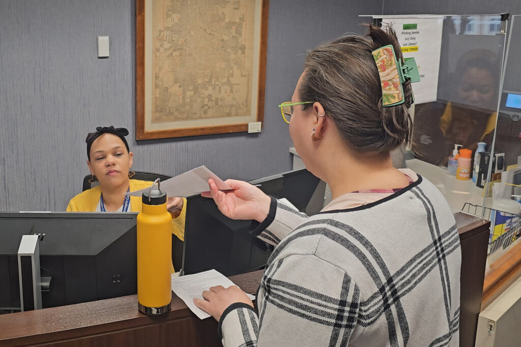 Natasha Villanueva hands a letter with the coalition’s demands to an administrative worker at the county office. Credit: Courtesy of Geoff Dittberner/Zero Burn Coalition