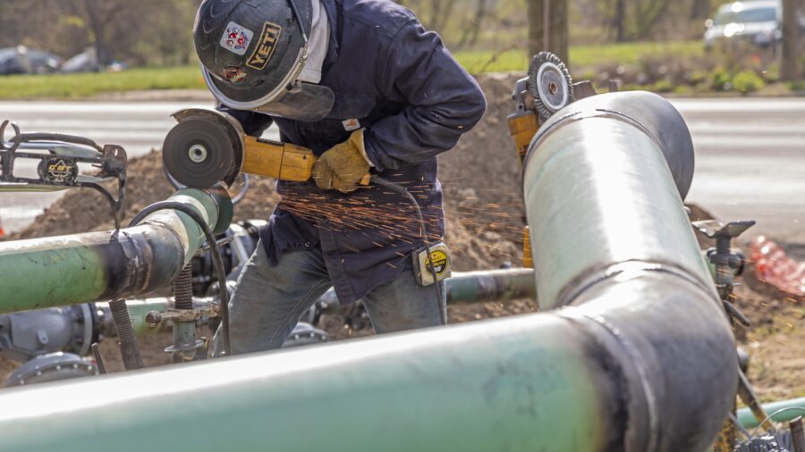 A worker in a hard hat leans over a pipe snaking over the ground.