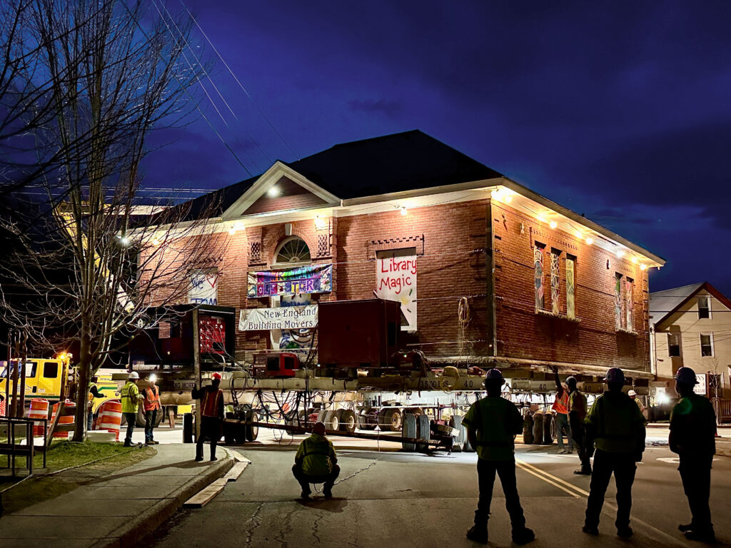 In this night shot, the library is lit up on its perch on a truck. One sign on the structure says, "Library Magic."