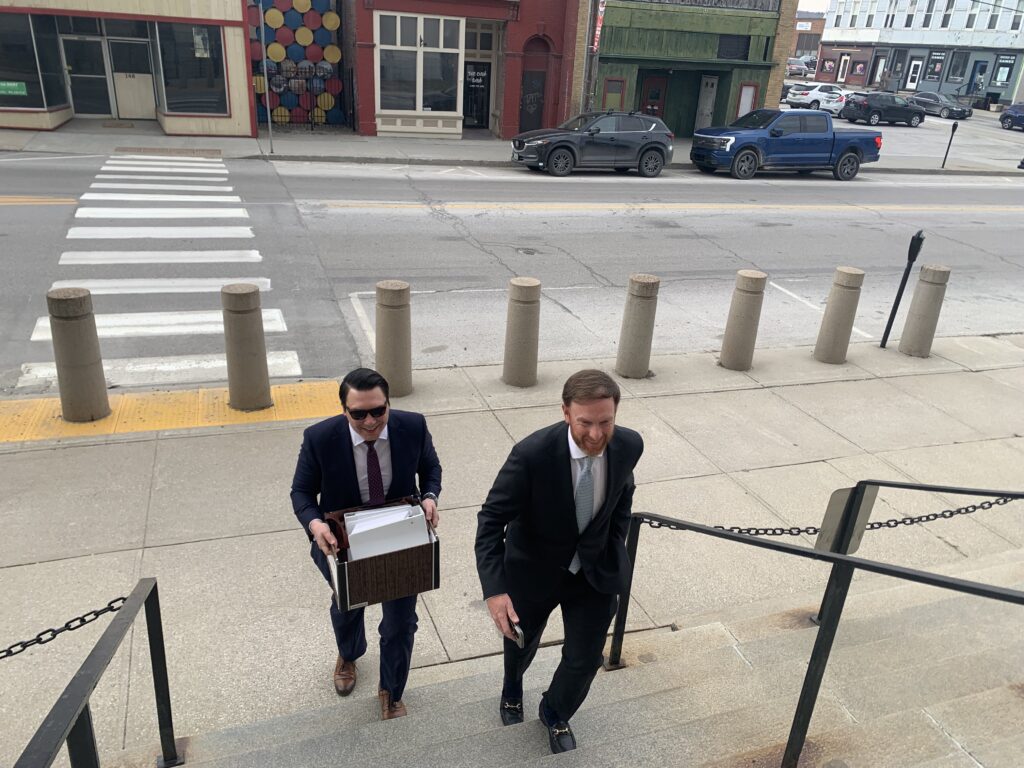The two men are walking up the stairs, one holding a file folder of documents.