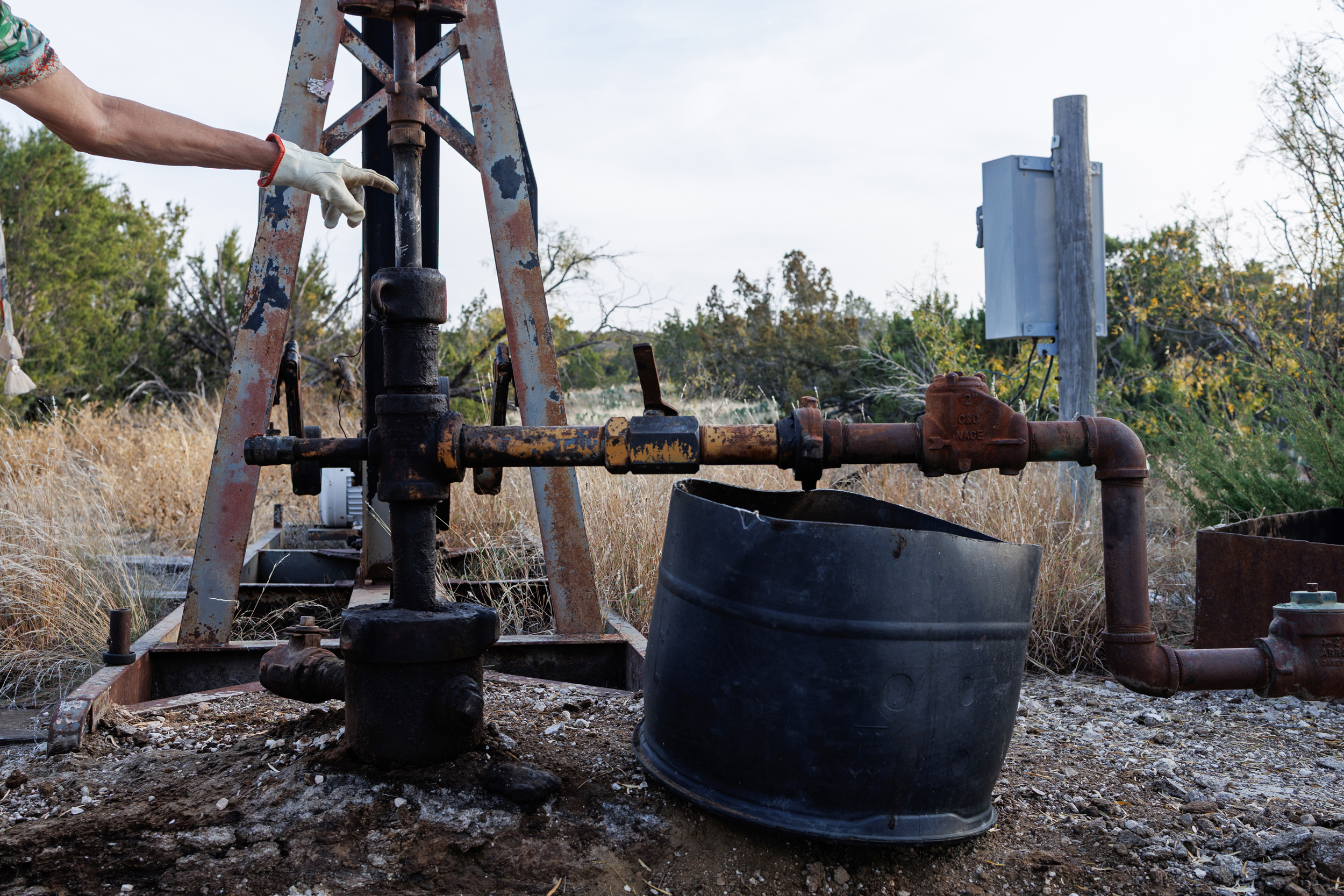 Jackie Chesnutt points to a leaking oil well operated by CORE Petro on her property near Knickerbocker, Texas.