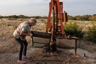 Jackie Chesnutt props up a sign next to a leaking oil well operated by CORE Petro on her property near Knickerbocker, Texas, on Nov. 18, 2025.