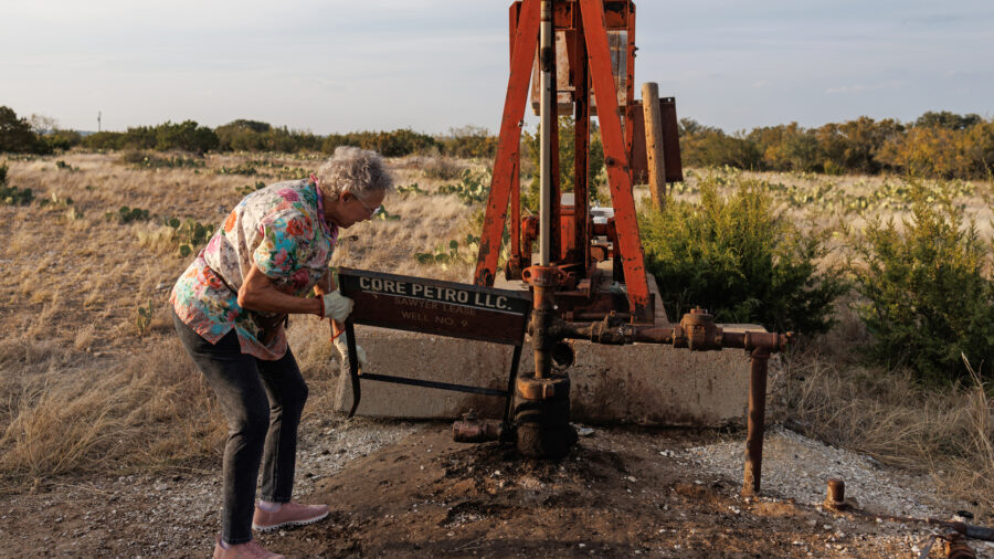 Jackie Chesnutt props up a sign next to a leaking oil well operated by CORE Petro on her property near Knickerbocker, Texas, on Nov. 18, 2025.
