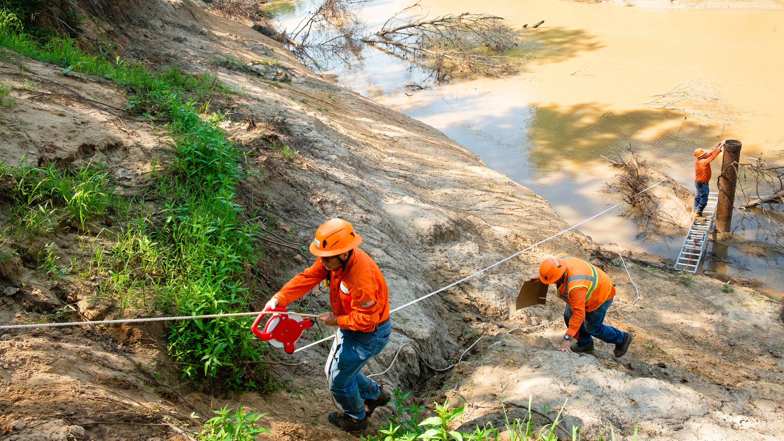 A team measures the distance from the riverbank as part of preparations for plugging the submerged well.
