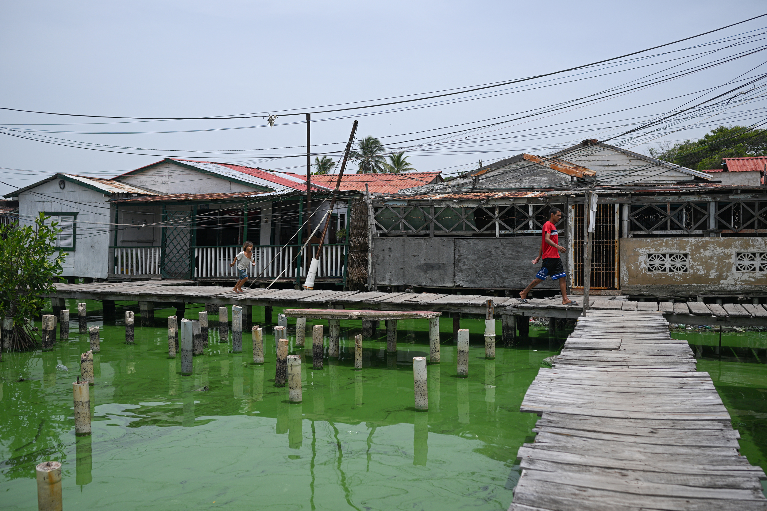 People walk past stilt houses in the Santa Rosa de Agua neighborhood in Maracaibo, Venezuela, as an oil slick covers the shores of Lake Maracaibo on July 11, 2024. Credit: Federico Parra/AFP via Getty Images