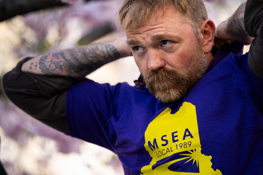Graham Platner puts on a union shirt during a May Day rally organized by local unions on May 1 outside City Hall in Portland, Maine. Credit: Graeme Sloan/Getty Images