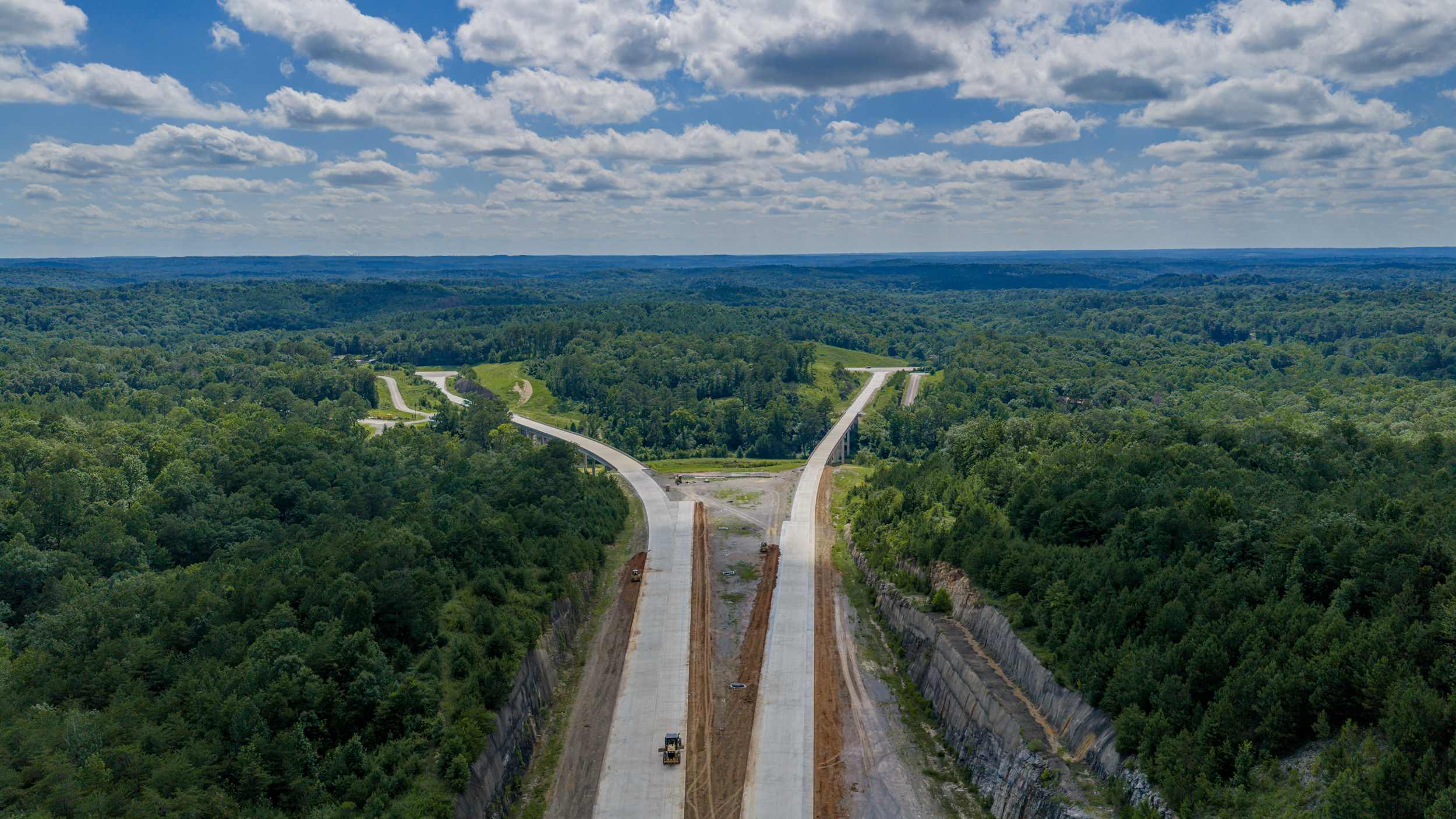 An aerial photo shows the highway construction cutting through a forest.