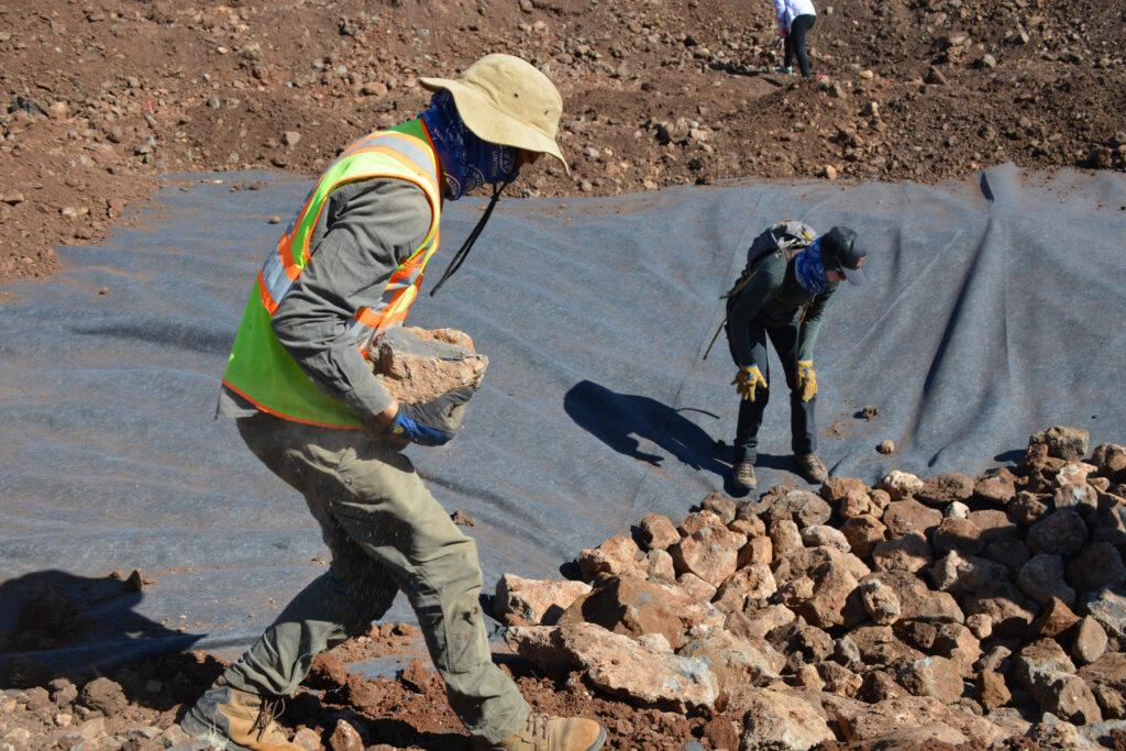 Volunteer Nate Evans places rocks atop an aquatic liner that, once finished, will create a pond and habitat for the threatened Chiricahua leopard frog. Credit: Wyatt Myskow/Inside Climate News
